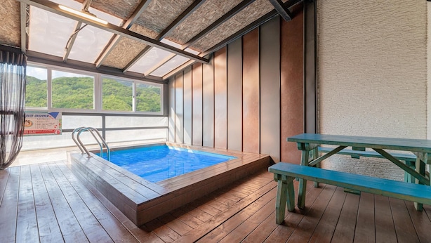 Eine Holzterrasse mit Whirlpool und Picknicktisch, große Fenster mit Blick auf Grünflächen und ein Schild in koreanischer Schrift.