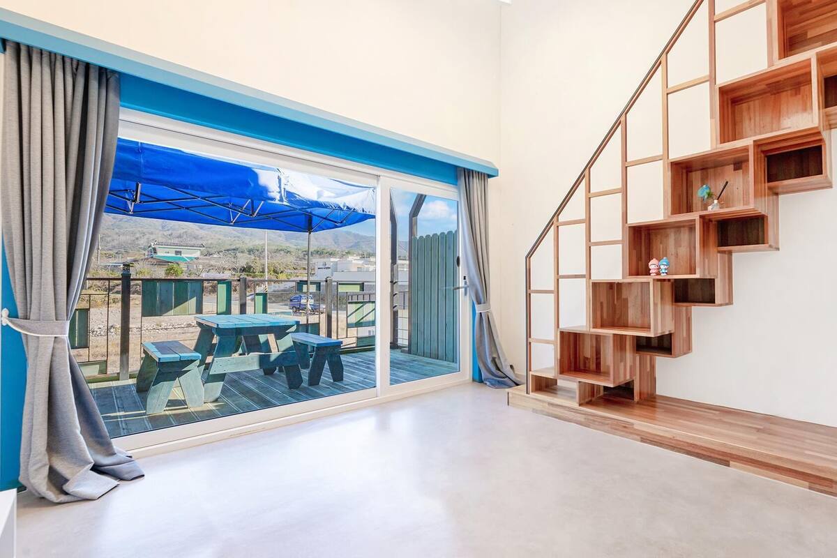 Ein modernes Interieur mit einer großen Schiebeglasdoor, die zu einer Terrassenauslässt, einer Holztreppe mit offenen Regalen und einem minimalistischen Design.