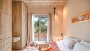 A bedroom with a large bed, a wooden wardrobe, a sliding glass door to a balcony, and a wall-mounted artwork. - Villa Aphrodite:Pet-friendly, 3 bedrooms,pool, WiFi, mobility-friendly (Poulades)