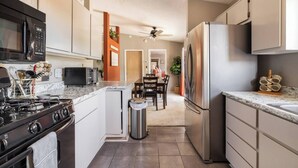 Una cocina moderna con estufa, microondas y refrigerador. Hay un comedor con sillas y una mesa.
