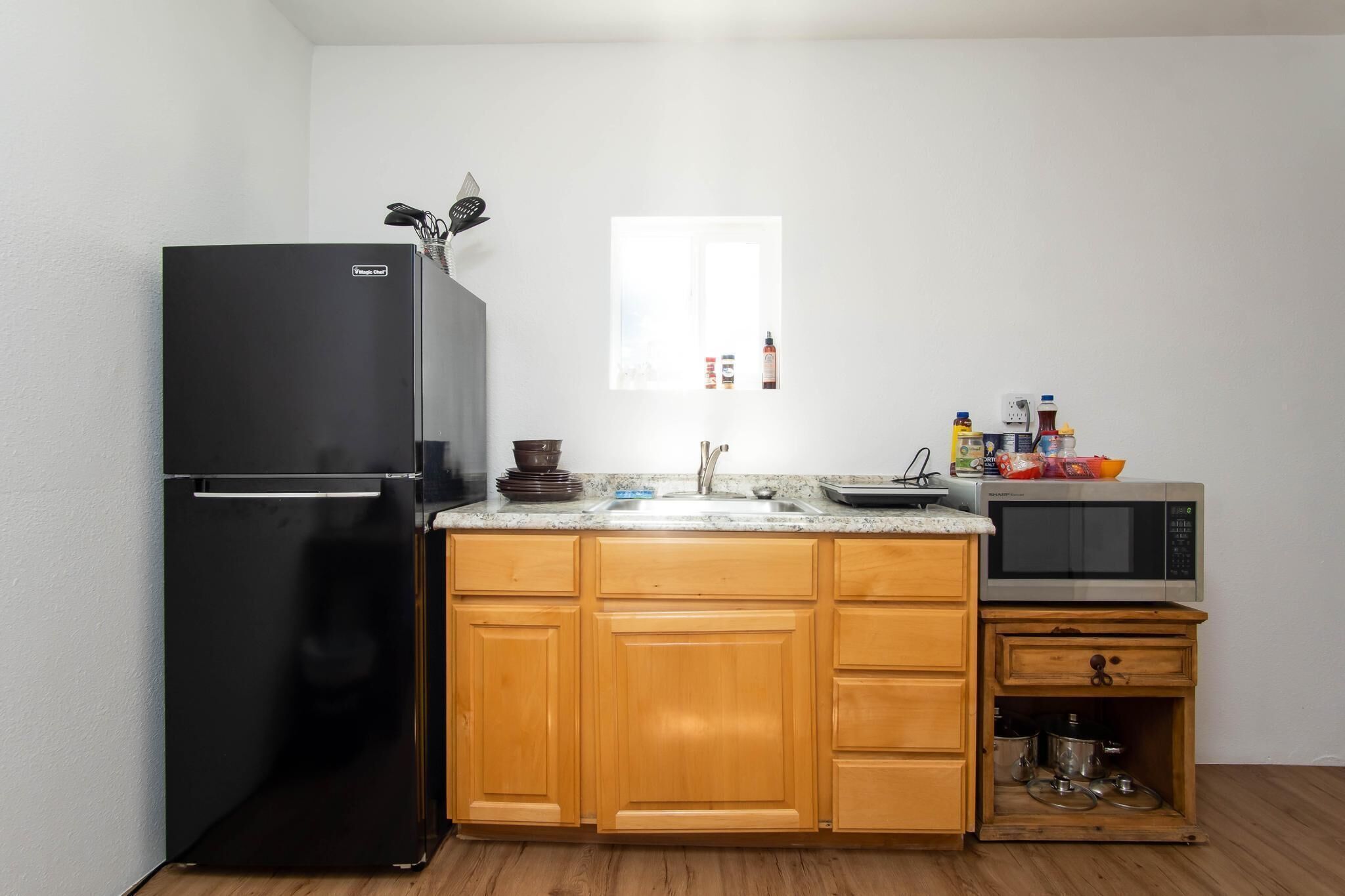 A compact kitchen with a black refrigerator, wooden cabinets, a sink, and a microwave.