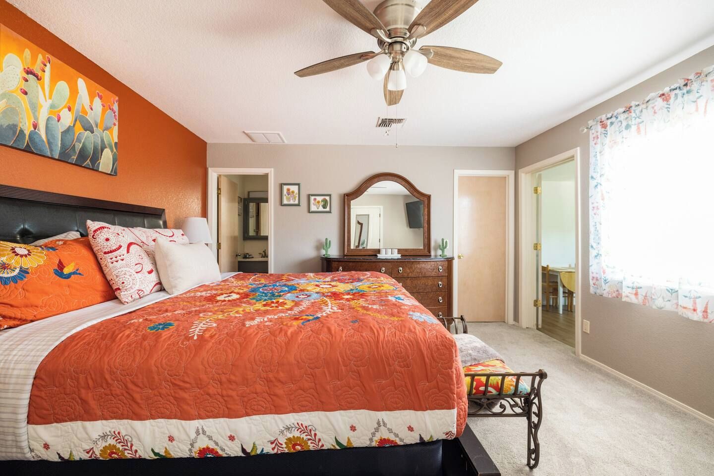 A bedroom with a large bed, a ceiling fan, a dresser, a mirror, and a window with curtains.