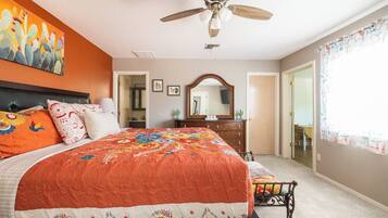 A bedroom with a large bed, a ceiling fan, a dresser, a mirror, and a window with curtains.