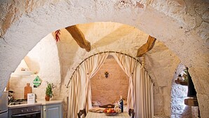 Un coin repas rustique avec un plafond en pierre, une table recouverte d’une nappe à carreaux et une bouteille de vin.