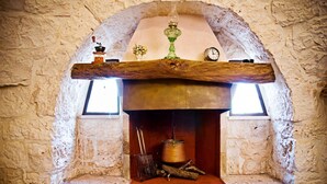 Une cheminée en pierre avec un manteau en bois, un vase en verre vert et une horloge.