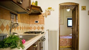 A kitchen with a stove, sink, and a radiator. There is a window in the adjacent room. - Dell'Aia: 1800s trullo house with garden view and ancient farmyard (Martina Franca)