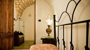 A bedroom with a bed, a wooden wardrobe, a lamp, and an arched doorway leading to another room. - Dell'Aia: 1800s trullo house with garden view and ancient farmyard (Martina Franca)