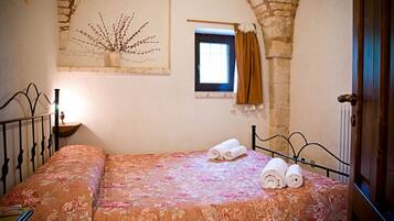 A bedroom with a bed, a window with curtains, a wall-mounted artwork, and a stone archway.