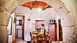 A rustic stone kitchen with a wooden ceiling, a dining table set with a plaid tablecloth, and a television on a wooden cabinet. - Dell'Aia: 1800s trullo house with garden view and ancient farmyard (Martina Franca)