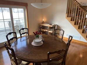 A dining area with a round wooden table, chairs, a vase with flowers, and a chandelier.
