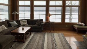 A cozy living room with a sectional sofa, a coffee table, and a view of a snowy landscape through large windows. - Gorgeous newer home on Newton Lake/Crystal Lake near Elk mountain ski resort.  (Greenfield Township)