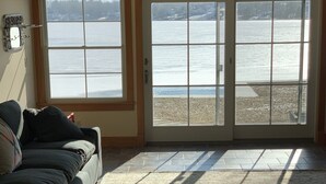 A living room with a sofa, a rug, and a view of a lake through large glass doors. - Gorgeous newer home on Newton Lake/Crystal Lake near Elk mountain ski resort.  (Greenfield Township)