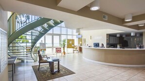 A spacious lobby with a curved reception desk, a staircase, and a view of the outdoors.