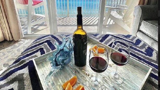 A balcony with a view of the ocean, a bottle of wine, and two glasses of wine on a table.