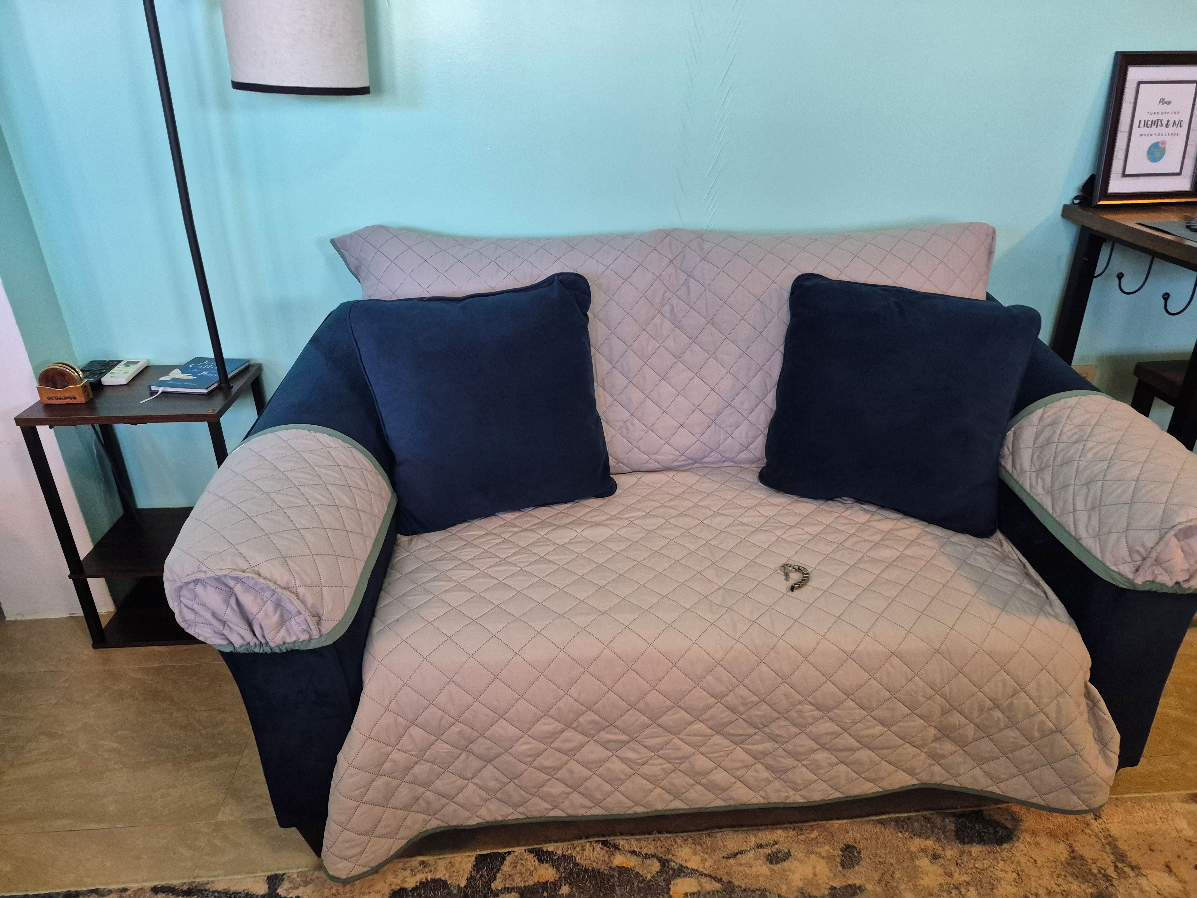 A bed with a quilted cover and two pillows, a bedside table with a lamp, and a framed picture on the wall.