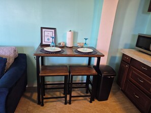 Un espai vital compacte amb taula de dinar, dues banquetes, un cubell de brossa i un televisor sobre un moble.