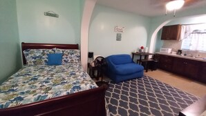 A bedroom with a bed, a blue chair, a kitchenette, and a ceiling fan. - Beautiful Apartment w- gorgeous expansive views, beautiful fruit trees & gardens (ST. THOMAS)