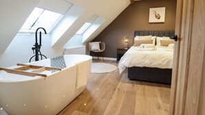 A bedroom with a large bed, a bathtub, and skylights. - Tyn Llwyn Barn (Corwen)