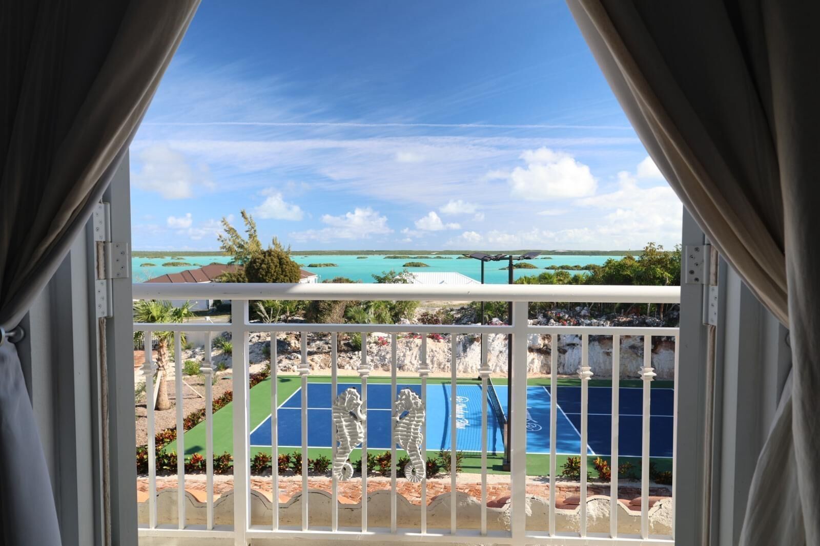 A balcony with a view of a beach, a pool, and a tennis court.