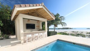 Eine Poolbar mit Fernseher, Barhocker und Blick auf den Strand.