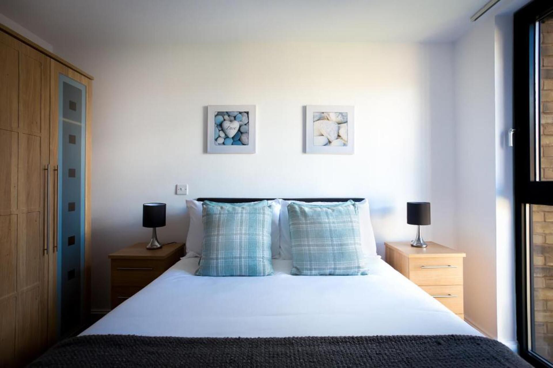 Une chambre à coucher comprenant un lit, deux tables de chevet, une armoire et deux œuvres d’art accrochées au mur.