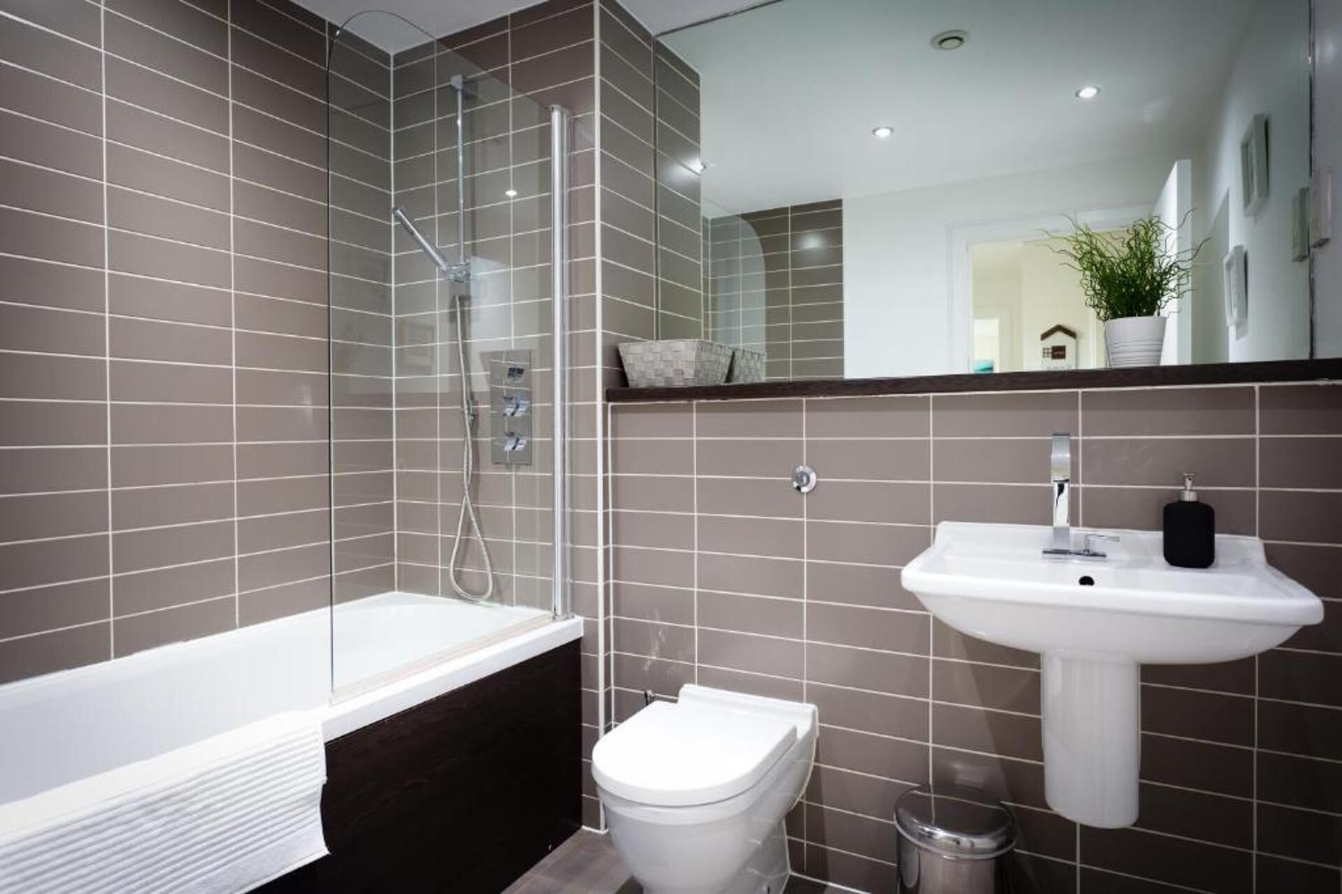 Une salle de bain moderne avec une douche à parois de verre, une baignoire blanche, des toilettes blanches et un lavabo blanc agrémenté d’un distributeur de savon noir.