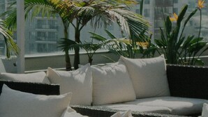 A balcony with a sofa, white cushions, and potted plants. - Modern Leopoldstadt 1BR w/ Rooftop & BBQ, near Metro U2, by Blueground (Vienna)