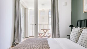 A bedroom with a bed, a nightstand, a lamp, and a view of an outdoor balcony.