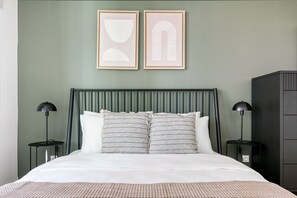 Un letto con una testiera verde, due lampade sui comodini e due opere d'arte astratte incorniciate appese al muro.