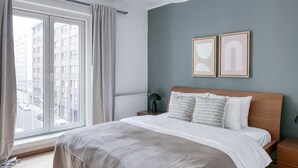 A bedroom with a large window, a bed with a wooden headboard, two framed pictures on the wall, and a bedside lamp. - Newly renovated Innere Stadt 1BR w/Elevator, near Metro U3, by Blueground (Vienna)