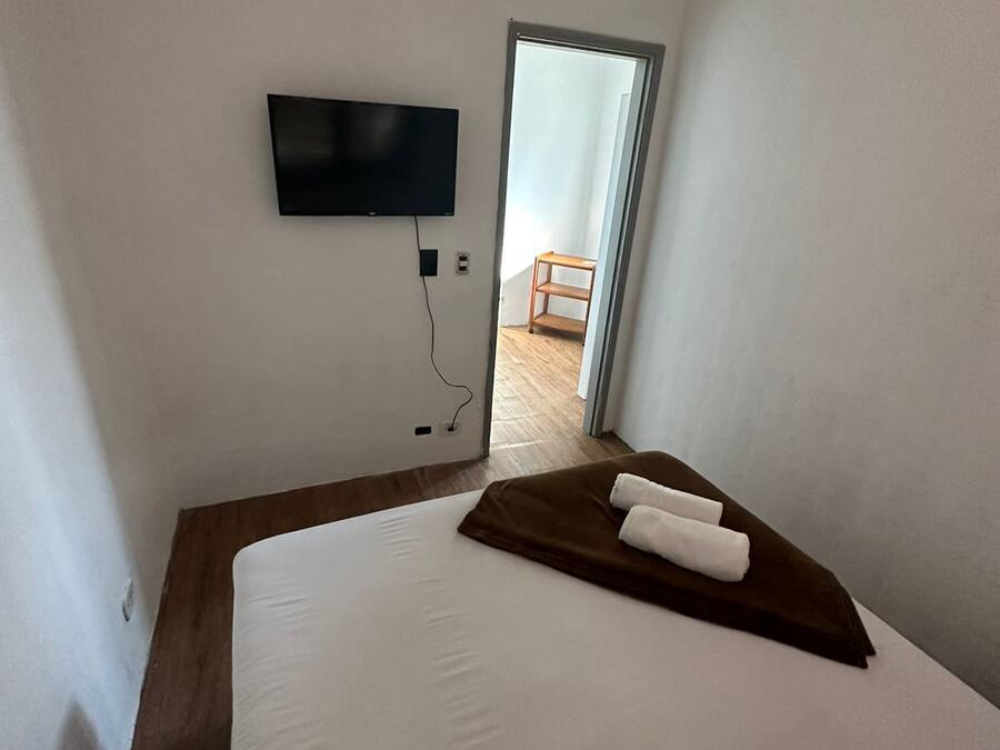 A hotel room with a bed, a TV mounted on the wall, and a door leading to a balcony.