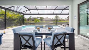 Un patio al aire libre con piscina, una mesa dispuesta para dos personas y una zona acristalada con vistas del paisaje circundante.