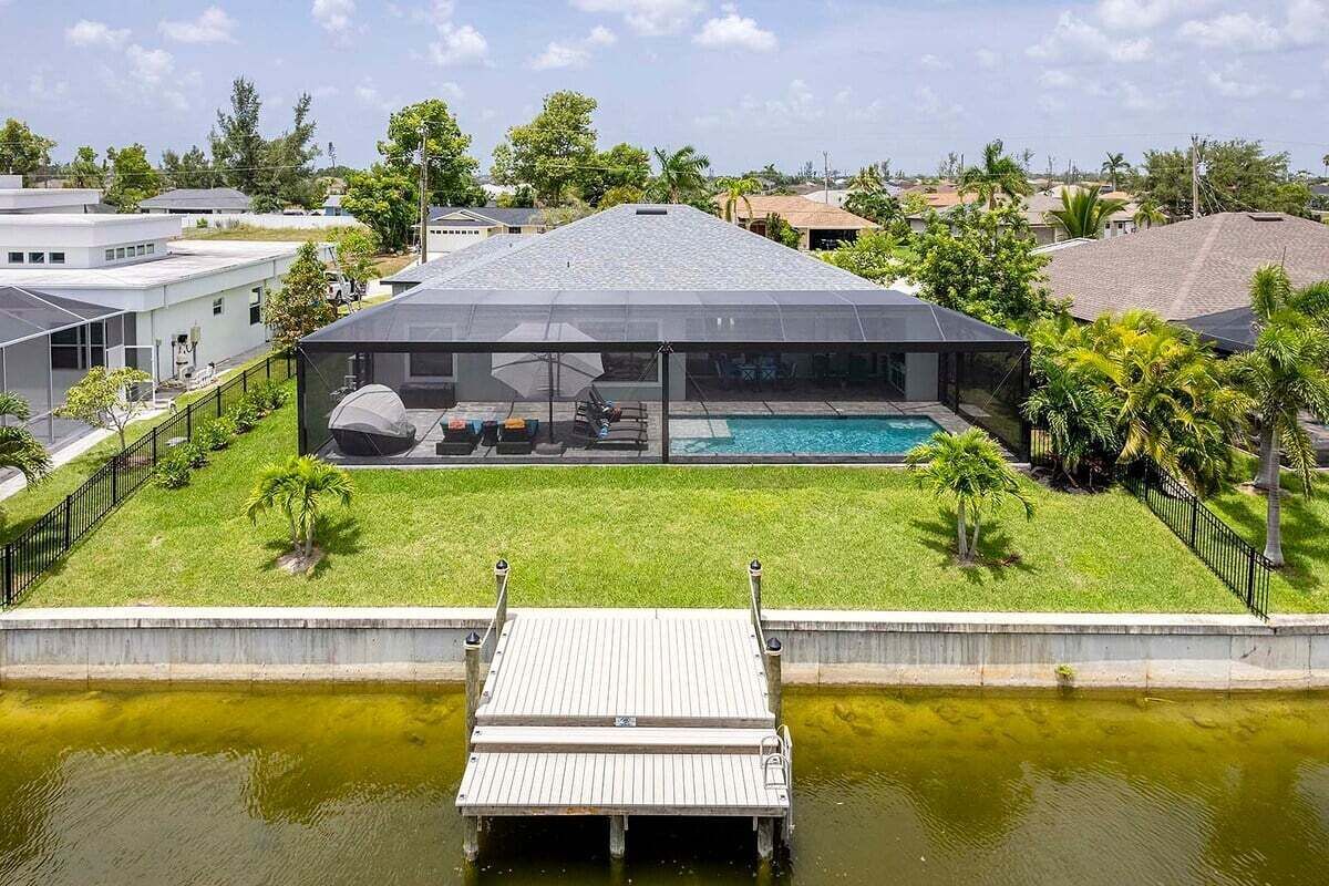 Ein modernes Haus mit Schwimmbad, überdachter Terrasse und einer an das Wasser führenden Anlegestelle.