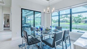 Un comedor moderno con una mesa de vidrio, sillas negras y vistas a un jardín exuberante a través de amplios ventanales.