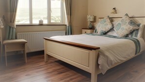 A bedroom with a wooden bed, a bedside table with a lamp, a chair, and a window with curtains. - Hilltop B&B (Carrigaholt)