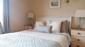 A neatly made bed with a quilted cover, two bedside tables with lamps, a wall-mounted painting, and a light fixture.