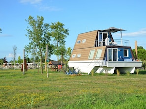 Ein modernes Hausboot mit flachem Dach, einem Balkon und einer überdachten Außenfläche.