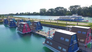 Ein schwimmendes Hausboot an einem Steg, mit einem Fluss und einem großen Boot im Hintergrund.