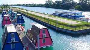 Ein Kanal mit schwimmenden Häusern, einer Bootsanlegestelle und einer Rasenfläche mit Menschen.