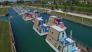 Une série de maisons flottantes, amarrées dans un canal, chacune ayant un design unique et plusieurs niveaux.