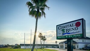 Letrero de Coastal Bend Motel & RV Park con una palmera en primer plano.