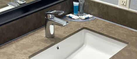 Une salle de bain avec un lavabo blanc, un miroir et des articles de toilette posés sur le comptoir.