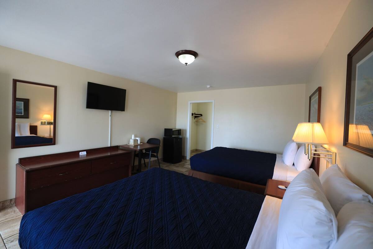 A hotel room with a large bed, a smaller bed, a desk with a chair, a television, and a mirror.