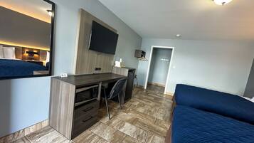 A compact hotel room with a bed, a desk, a chair, a flat-screen TV, and a microwave.
