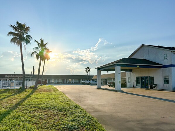 A motel with a covered parking area, palm trees, and a building with a '201' sign.