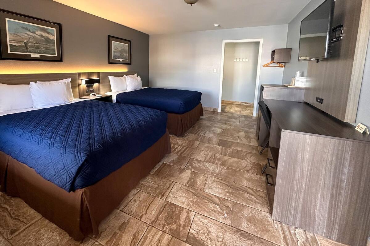 A hotel room with two beds, a desk, a mirror, and a door leading to a bathroom.