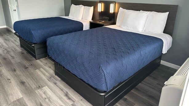 Una cama doble con cabecera oscura y dos mesitas de noche, cada una con una lámpara.