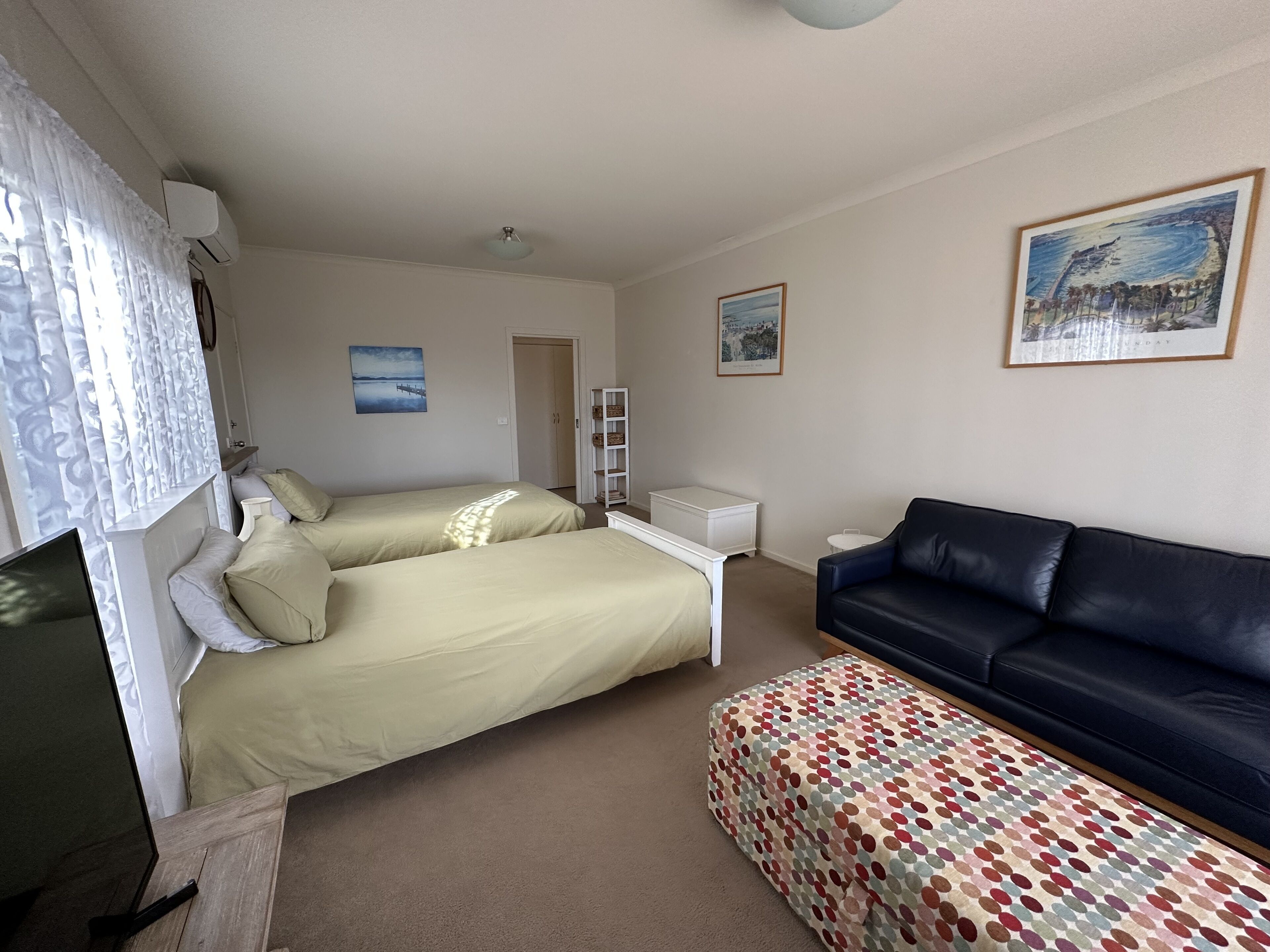 A bedroom with two beds, a sofa, a small table, and a patterned ottoman.