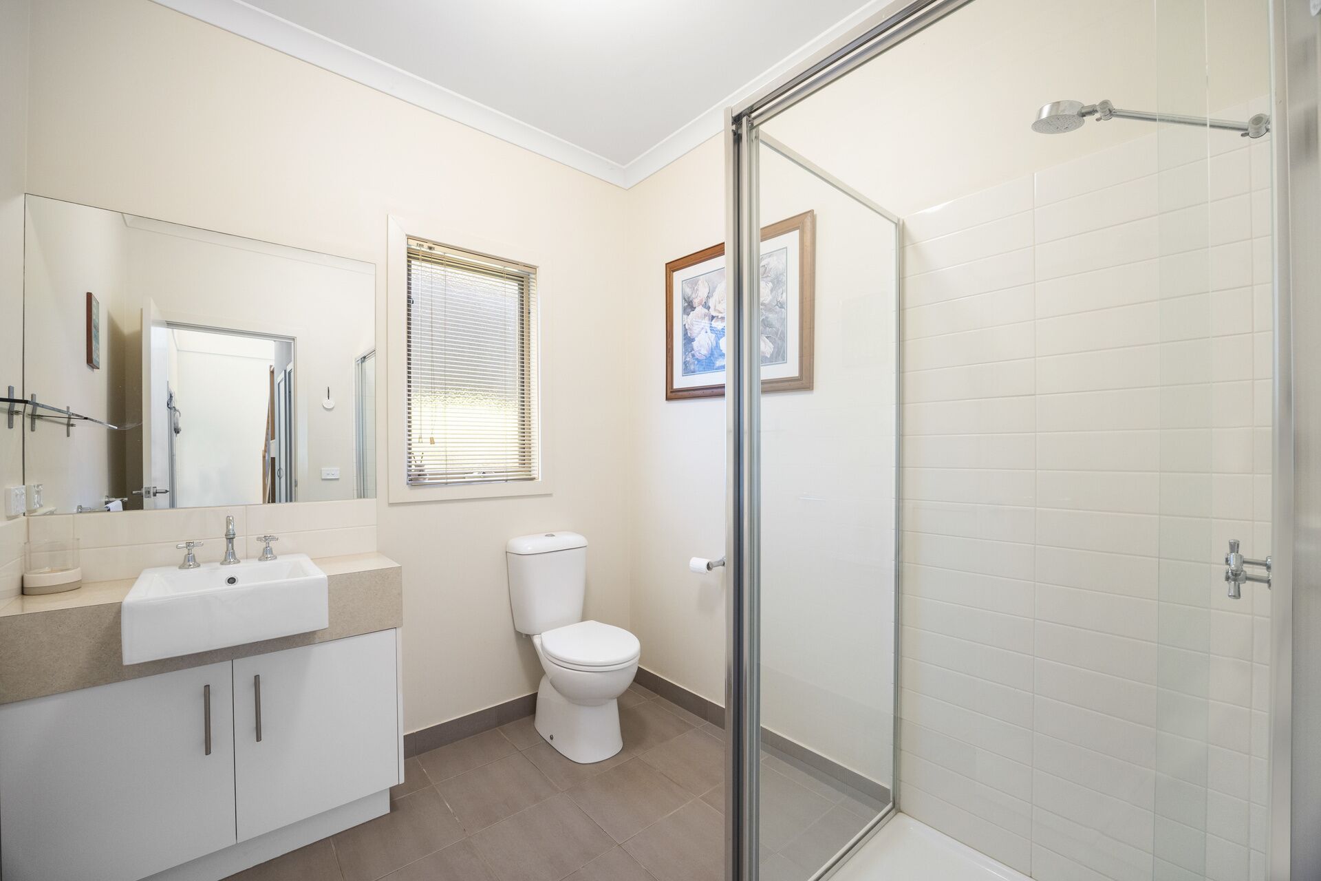 A modern bathroom with a glass shower enclosure, a toilet, and a sink with a mirror above it.