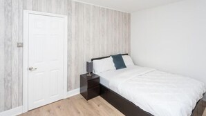 Een slaapkamer met een bed, een nachtkastje, een witte deur en een lamp aan het plafond.